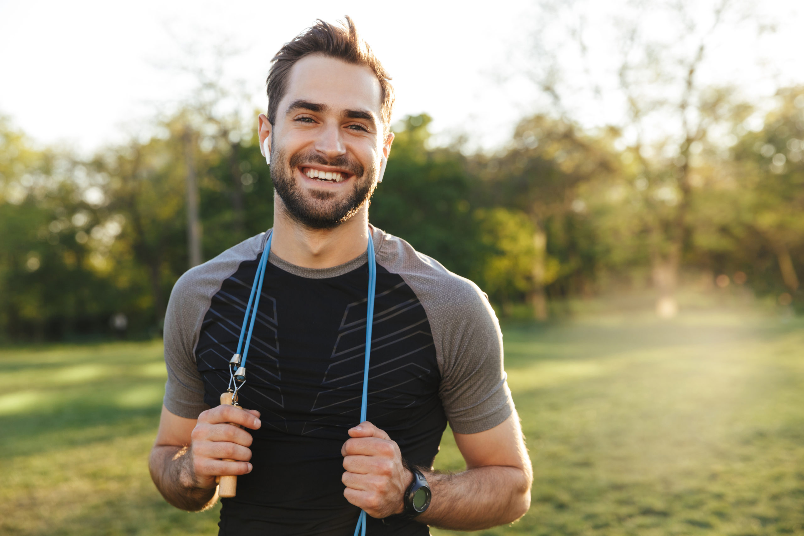 Handsome young strong sports man posing outdoors at the nature park location with skipping rope.