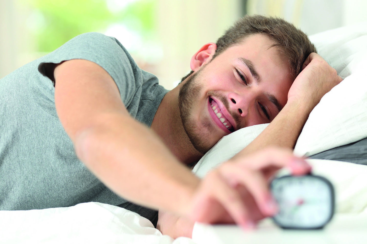 Happy man waking up turning off alarm clock