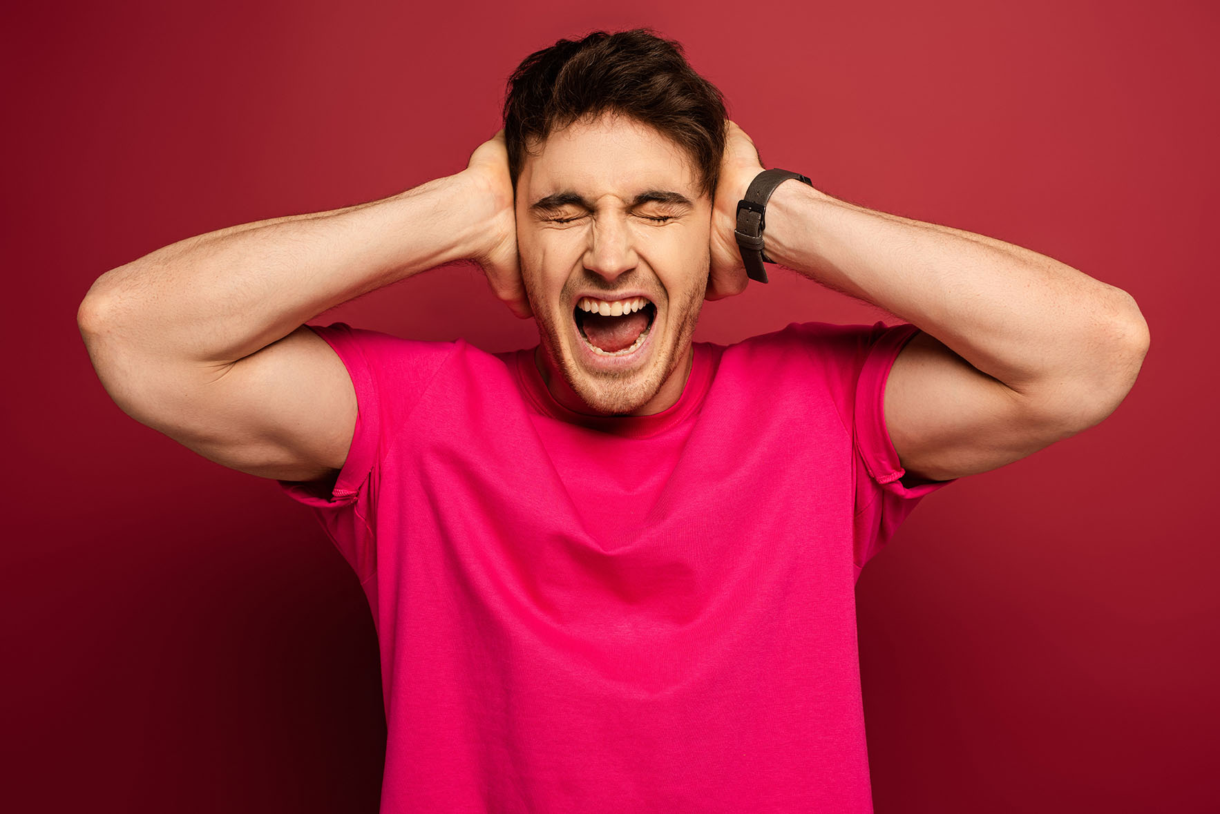 portrait of smiling man shouting and covering ears on red